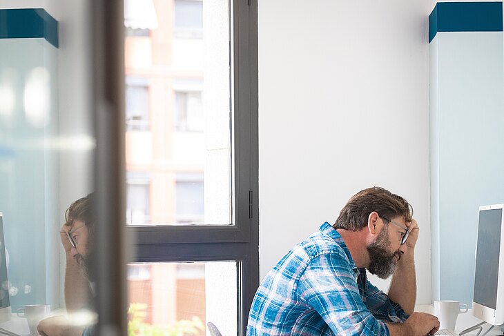 Grübelnder Mitarbeiter sitzt vor einem Computermonitor