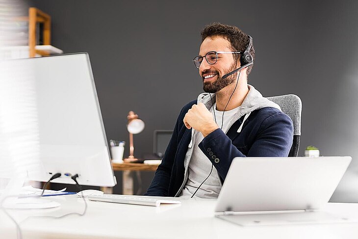 Teilnahme an einer Online-Schulung des Deutschen Ausschreibungsblatts Mann mit Headset schaut lächelnd auf einen Bildschirm