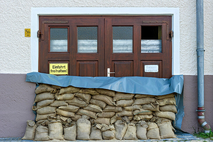 Ein Eingang mit Holztüren ist mit Sandsäcken und einer blauen Plane vor Hochwasser geschützt